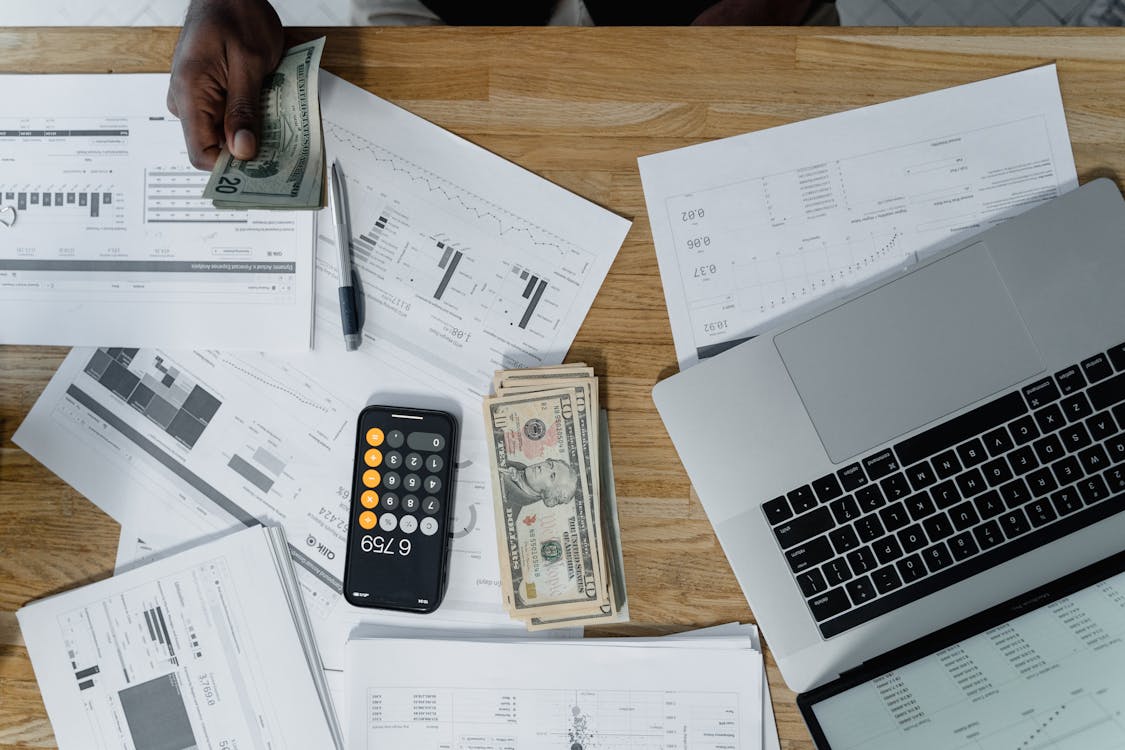 Free Overhead view of a busy workspace with cash, financial documents, and a laptop. Stock Photo